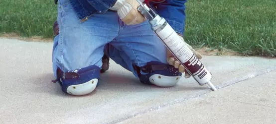 Kneeling construction worker applies parking structure sealants FC and SL to joint in concrete sidewalk. Parking structure sealants Construction Industry/SealantsProduct brochure