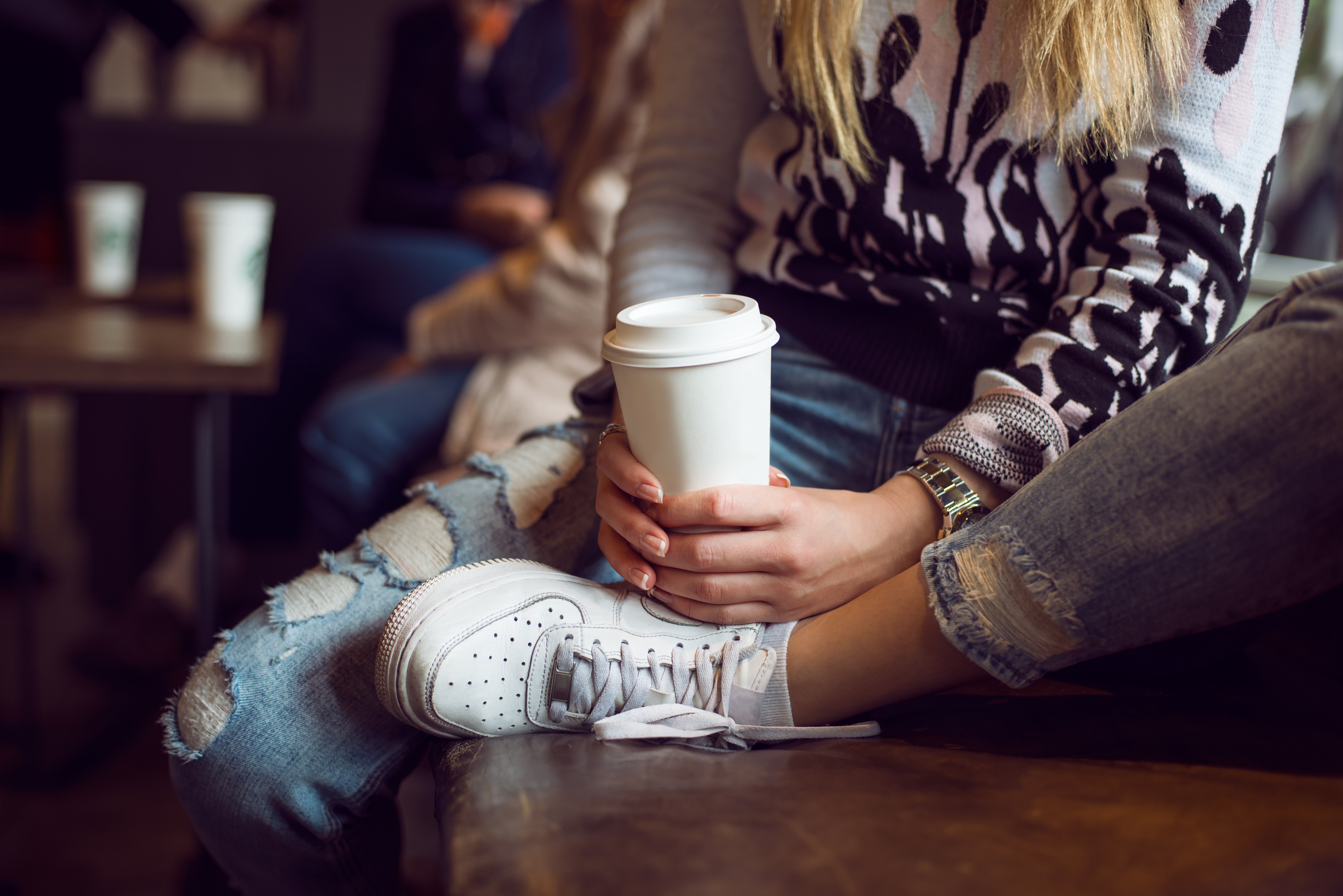 A woman holds a paper coffee cup while sitting in a café