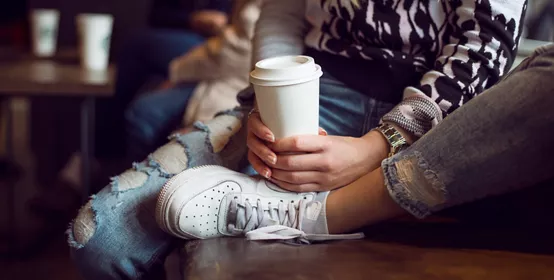 Two people sitting holding a paper coffee cup 
