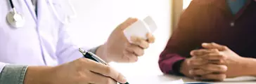 Doctor holding a pill bottle and writing while talking with a patient
