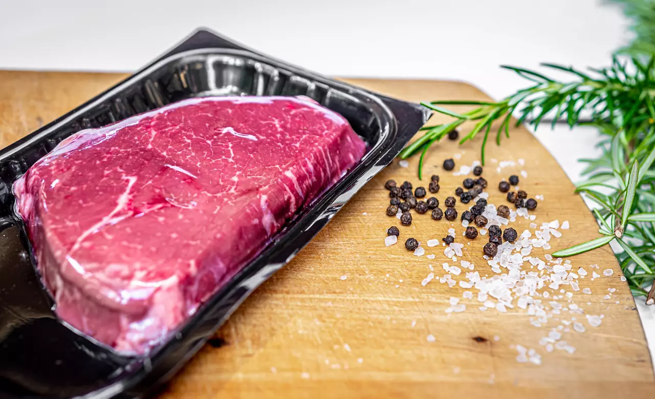 Beef steak in vacuum skin packaging and spices on wooden chopping board with copyspace