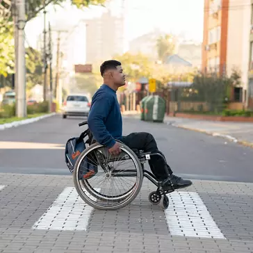 Profile of man in wheelchair crossing street at crosswalk 