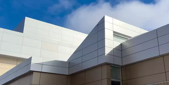 Commercial external metal composite panels on a building with blue sky and clouds in the background. The durable metal composite panels are two shades of grey in color on the modern building.