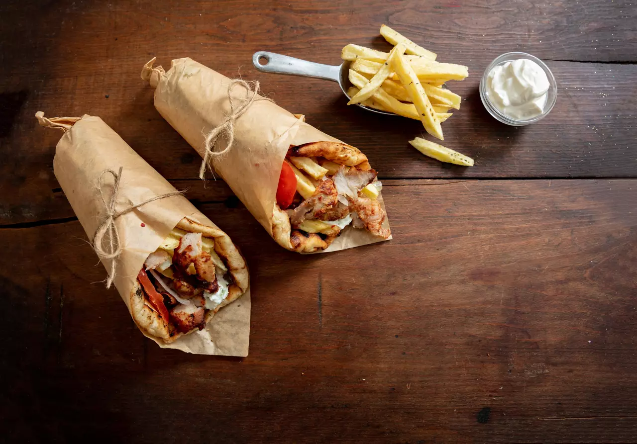 Shawarma Gyro pita on wooden table. Greek food, sliced meat, potato, tomato and tzatziki, paper wrap, top view, copy space.